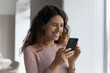 © fizkes - Happy millennial Latino woman hold cellphone look at screen browse wireless internet on gadget. Smiling Hispanic female use smartphone talk speak on video webcam online virtual call on modern device.