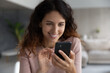 © fizkes - Happy millennial Hispanic woman hold smartphone look at screen speak talk on video webcam virtual call online. Smiling young Latino female use cellphone text message on modern electronic device.