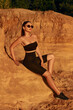 © Dmitry Tsvetkov - Young sexy sporty caucasian tanned woman with pony tail brunette hair in black shorts and top sitting against sand wall at sunset. Fashion female model