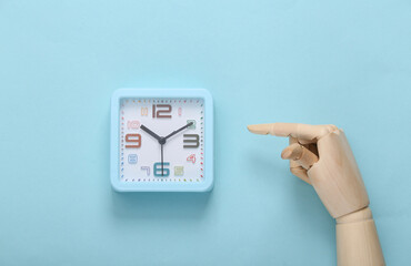 Wall Mural - Wooden hand points to an alarm clock on blue background