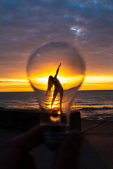 Wall Mural - a man holds up a lightbulb in front of a woman's silhouette with angled outstretched arms and body o