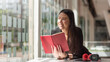 © amnaj - Beautiful Asian businesswoman holding a book headphone a clock on the office desk.