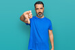 © Krakenimages.com - Middle aged man with beard wearing casual blue t shirt looking unhappy and angry showing rejection and negative with thumbs down gesture. bad expression.