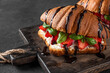 French croissant sandwiches with fresh strawberries, cream cheese, basil and chocolate sauce on dark background. close up