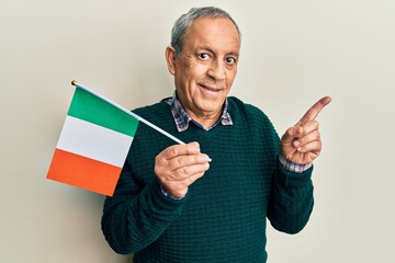 Poster - Handsome senior man with grey hair holding ireland flag smiling happy pointing with hand and finger to the side