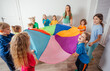 © oksix - Teacher and kindergarten kids playing with colorful parachute
