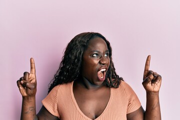 Sticker - African young woman pointing up with fingers angry and mad screaming frustrated and furious, shouting with anger. rage and aggressive concept.