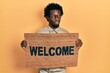 Young african american man holding welcome doormat smiling looking to the side and staring away thinking.