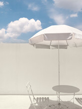 White Beach Umbrella, Table And Chairs With Blue Sky And White Wall.
