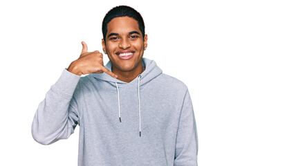 Young handsome hispanic man wearing casual sweatshirt smiling doing phone gesture with hand and fingers like talking on the telephone. communicating concepts.