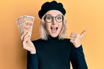 Sticker - Young blonde girl holding 50 turkish lira banknotes pointing thumb up to the side smiling happy with open mouth