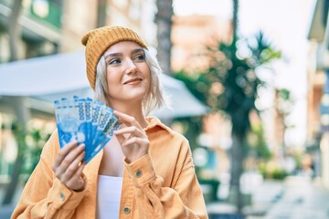 Wall Mural - Young blonde girl smiling happy counting chilean pesos banknotes at the city.