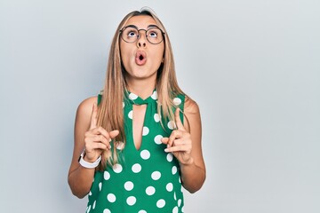 Canvas Print - Beautiful hispanic woman wearing elegant shirt and glasses amazed and surprised looking up and pointing with fingers and raised arms.