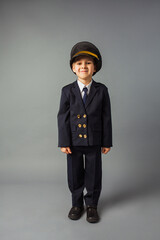 Wall Mural - Boy dressed in a black pilot uniform stands at the gray background