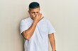 Young latin man wearing casual white t shirt smelling something stinky and disgusting, intolerable smell, holding breath with fingers on nose. bad smell