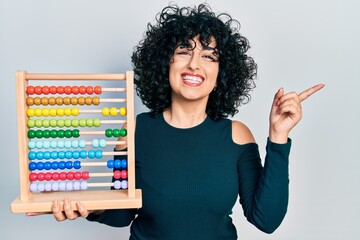 Sticker - Young middle east woman holding traditional abacus smiling happy pointing with hand and finger to the side