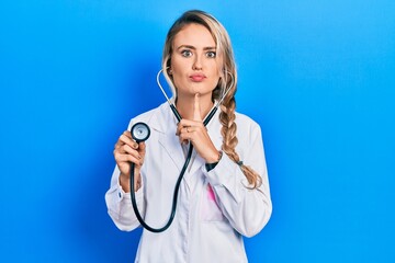 Sticker - Beautiful young blonde doctor woman holding stethoscope thinking concentrated about doubt with finger on chin and looking up wondering