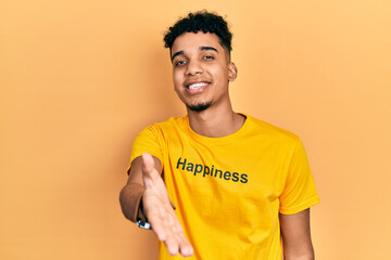 Young african american man wearing t shirt with happiness word message smiling cheerful offering palm hand giving assistance and acceptance.