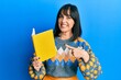 © Krakenimages.com - Young hispanic woman reading book smiling happy pointing with hand and finger