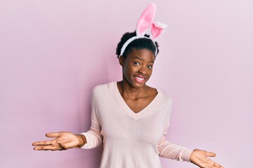 Canvas Print - Young african american girl wearing cute easter bunny ears clueless and confused expression with arms and hands raised. doubt concept.