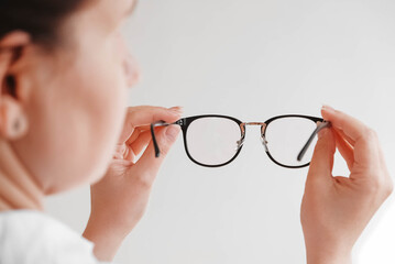 Woman holding optical glasses in a black frame on a white background. Copy, empty space