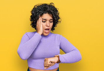 Young hispanic woman with curly hair wearing casual clothes looking at the watch time worried, afraid of getting late