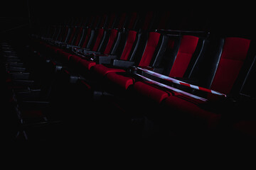 Wall Mural - Empty movie theater. Armchairs red and black in the cinema hall are illuminated by a beam of light, low key. Selective focus. Quarantine, restrictive tape on chairs