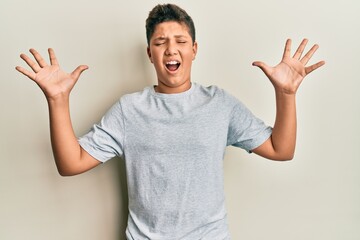 Wall Mural - Teenager hispanic boy wearing casual grey t shirt celebrating mad and crazy for success with arms raised and closed eyes screaming excited. winner concept