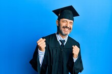 Middle Age Hispanic Man Wearing Graduation Cap And Ceremony Robe Very Happy And Excited Doing Winner Gesture With Arms Raised, Smiling And Screaming For Success. Celebration Concept.
