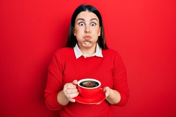 Canvas Print - Young hispanic woman drinking a cup of coffee puffing cheeks with funny face. mouth inflated with air, catching air.