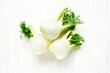 Fresh Florence fennel bulbs on white wooden background. Raw organic spring vegetables top view. Genuine healthy eating.