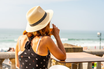 Summer vacation lifestyle. Young caucasian girl in a hat having a soda next to the beach and looking at the sea