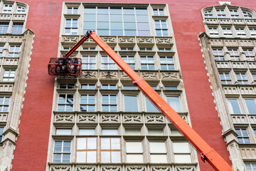 Professional high rise window cleaning service workers on the platform of telescopic boom lift. Two workers use specialized equipment to access and clean windows of residential building