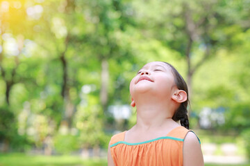 Portrait of happy Asian child close their eyes in garden with Breathe fresh air from nature. Close up kid girl relax in green park for good health.