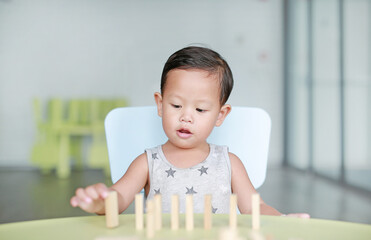 Portrait of little baby boy playing wood blocks tower game for Brain and Physical development skill in a classroom. Focus at children face. Child learning and mental skills concept.