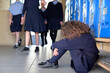 Sad young schoolgirl sitting alone in school corridor floor being bullied