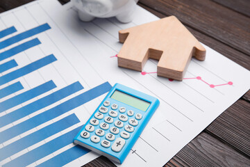 Wall Mural - Calculator with house figure and charts on wooden background, closeup