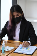 Wall Mural - Businesswoman in protective mask analyzing business data at office.