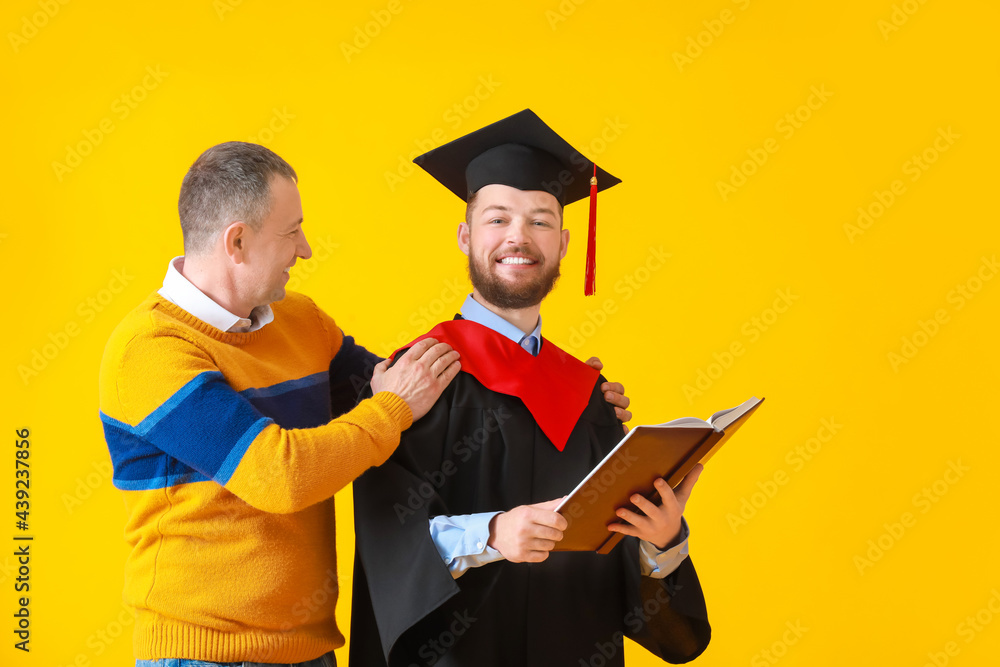 Happy male graduation student with his father on color background