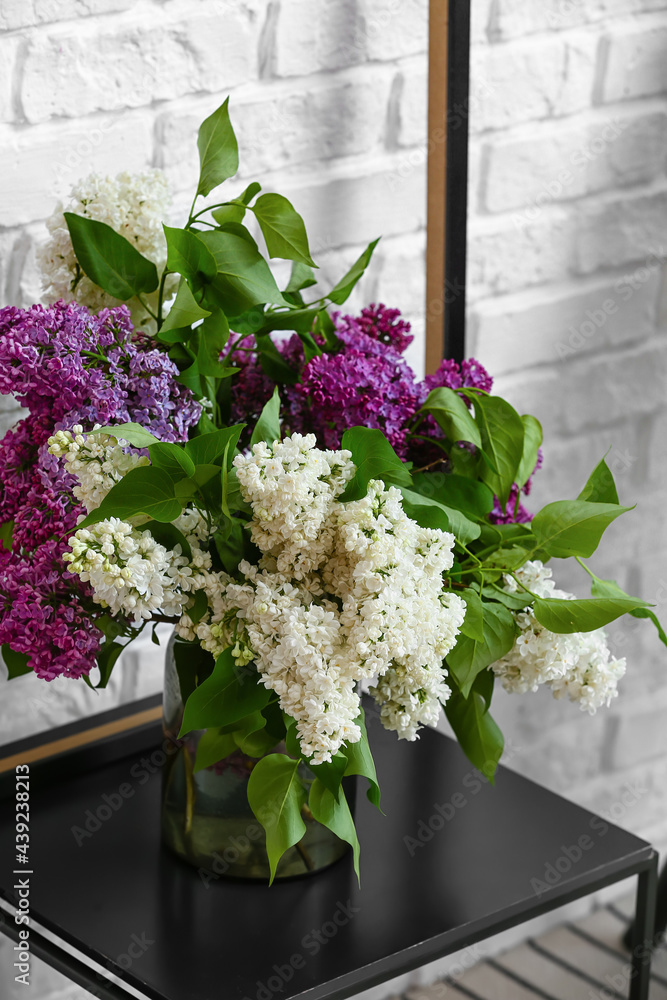 Vase with lilac flowers on table near brick wall