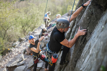 Senior man with instructor climbing rocks outdoors in nature, active lifestyle.