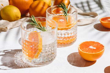 Summer orange cocktails with citrus fruits on white background. Hard seltzer, lemonade, refreshing drinks, low alcohol mocktails, summer party concept. Trendy palm leaf shadow and sunlight, sun.