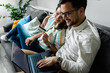 © Zoran Zeremski - Smiling couple sitting on sofa at home using laptop for shopping online.