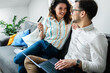 © Zoran Zeremski - Smiling couple sitting on sofa at home using laptop for shopping online.