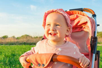 Wall Mural - Little baby girl sitting in a stroller and smiling cute.