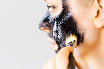 Woman applying black mask to skin face