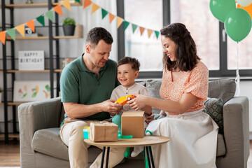 Wall Mural - family, holidays and people concept - happy mother, father and little son opening birthday presents at home party