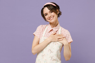 Young fun thankful kind-hearted housewife housekeeper chef cook baker woman wear pink apron put folded hands on heart isolated on pastel violet color background studio portrait. Cooking food concept