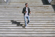 © ViDi Studio - Full length smiling young man in black leather jacket glasses walk in city downtown go down concrete steps hold mobile cell phone takeaway craft paper cup drink coffee to go Urban lifestyle concept.