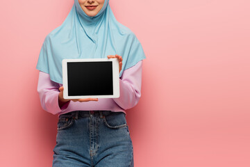 Wall Mural - partial view of smiling muslim woman holding digital tablet with blank screen on pink